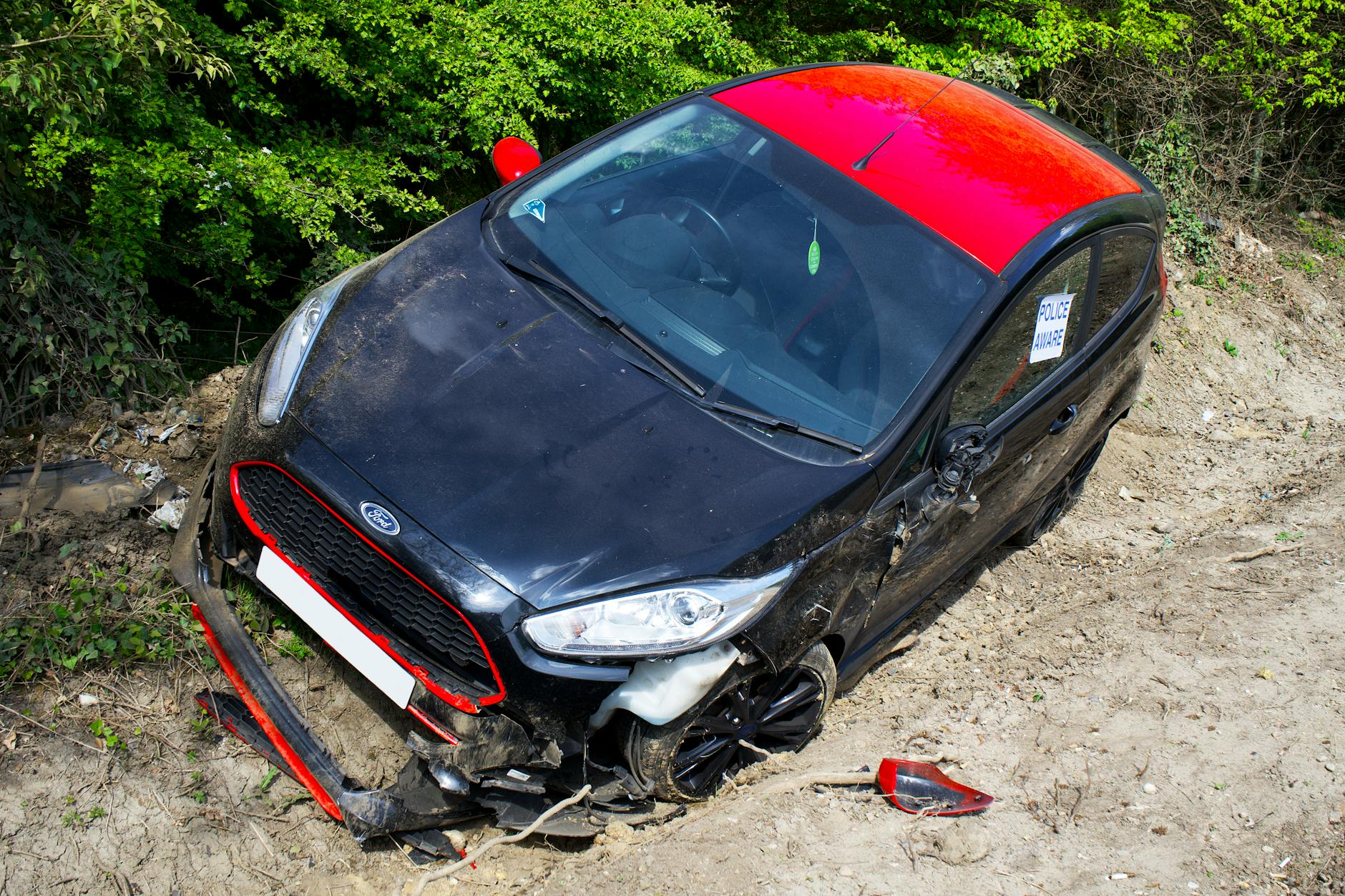 Rozbity czarno‑czerwony Ford Fiesta stojący poza drogą