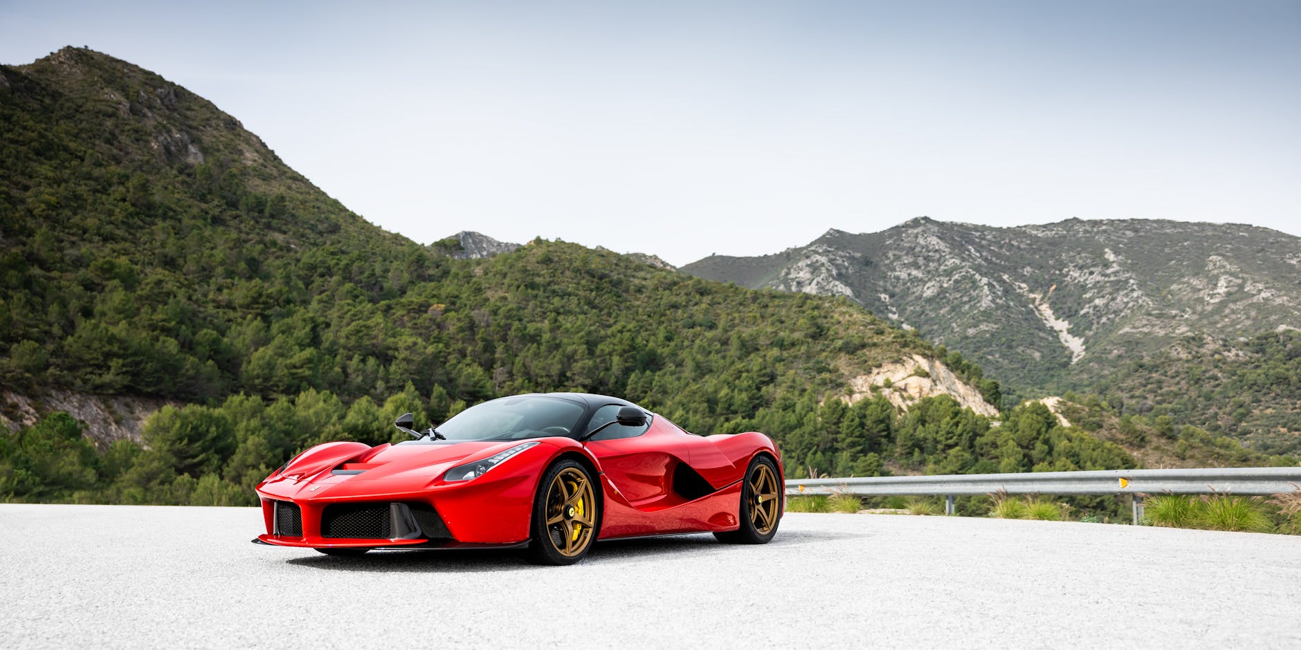 Czerwone sportowe auto zaparkowane na górskiej drodze wśród zieleni