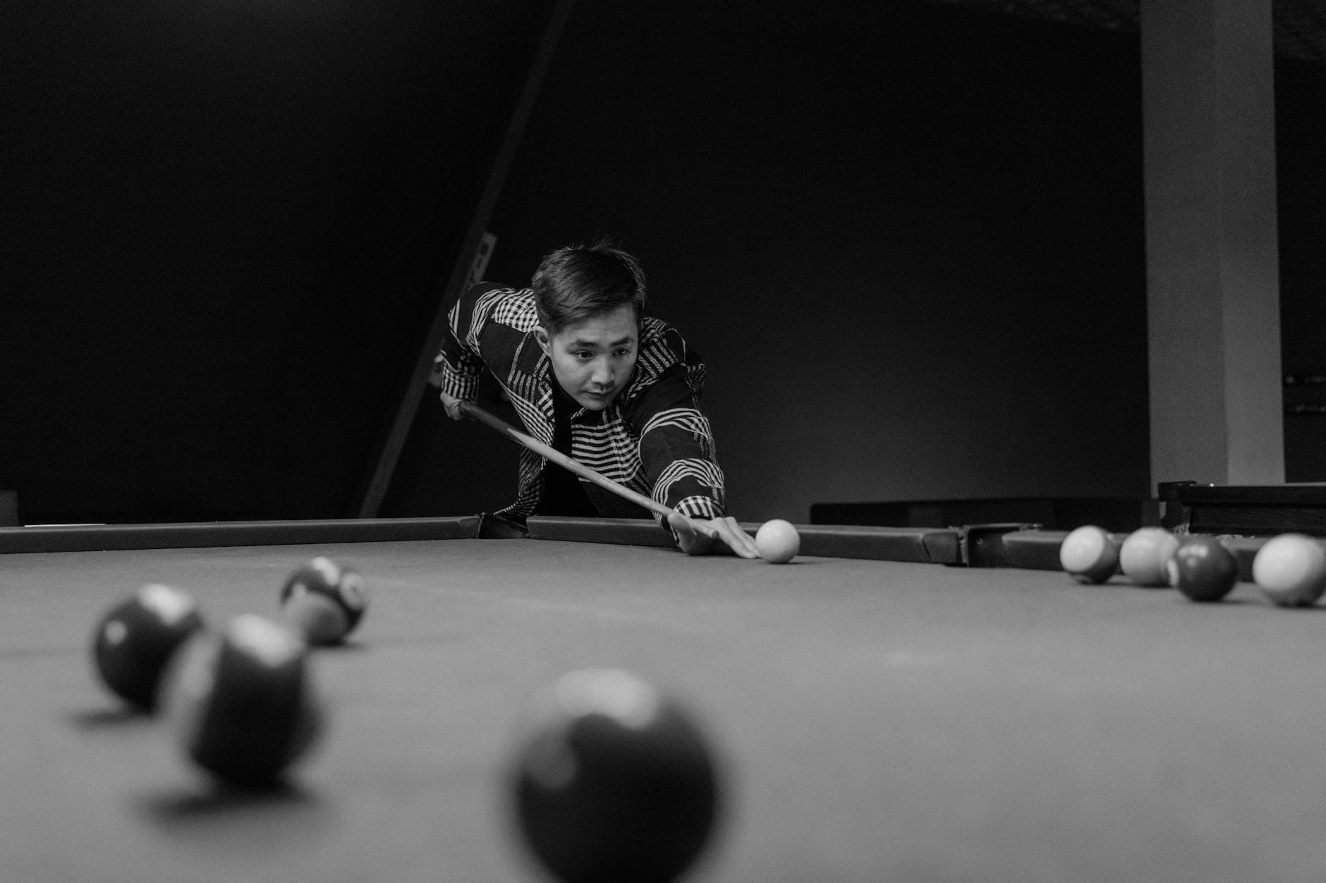 Mężczyzna z kijem bilardowym celujący do uderzenia w czarno-białym kadrze