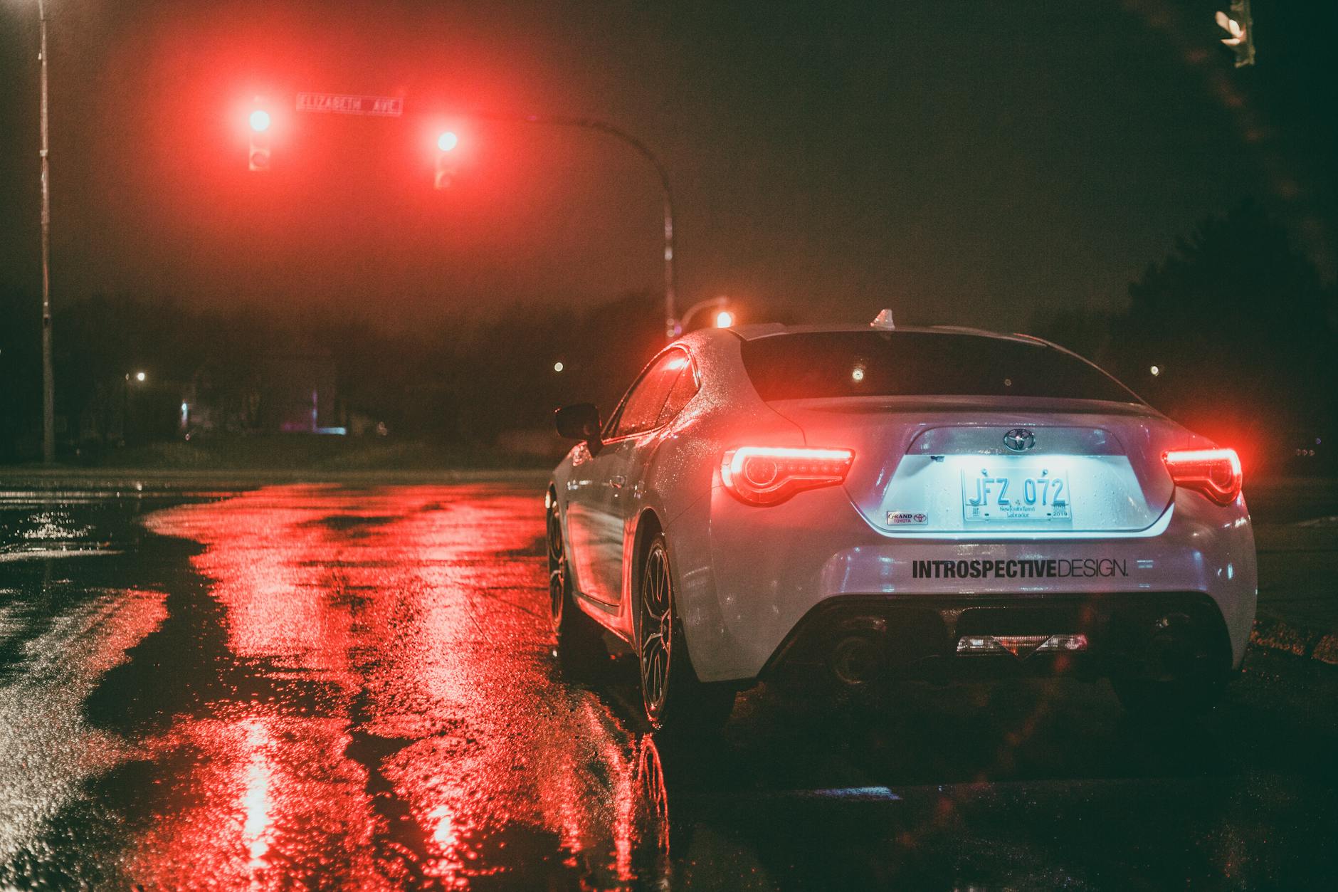 Białe auto czeka na czerwonym świetle na mokrym, nocnym skrzyżowaniu