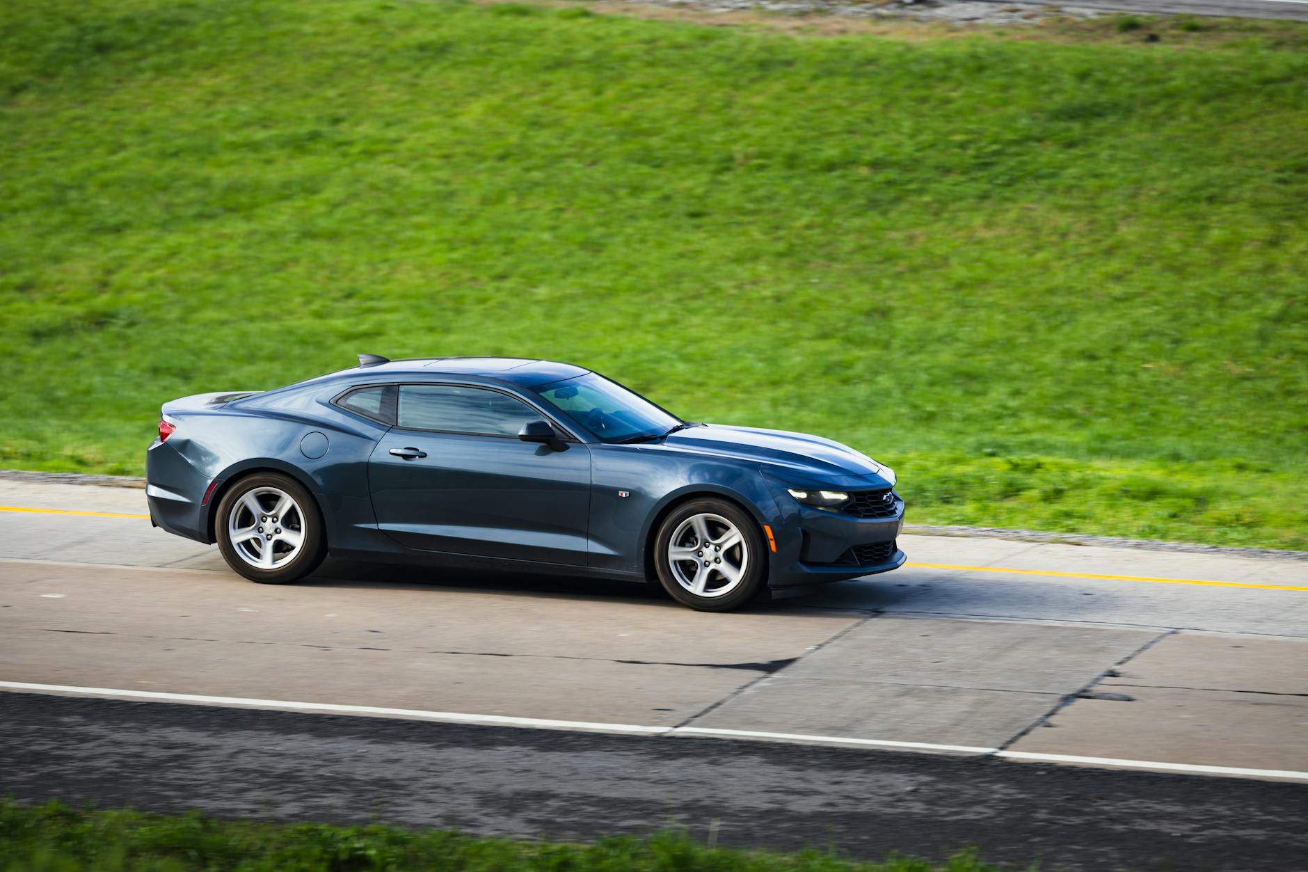 Czarny sportowy samochód jedzie szybko po gładkiej szosie między polami Czarny sportowy samochód jedzie szybko po gładkiej szosie między polami