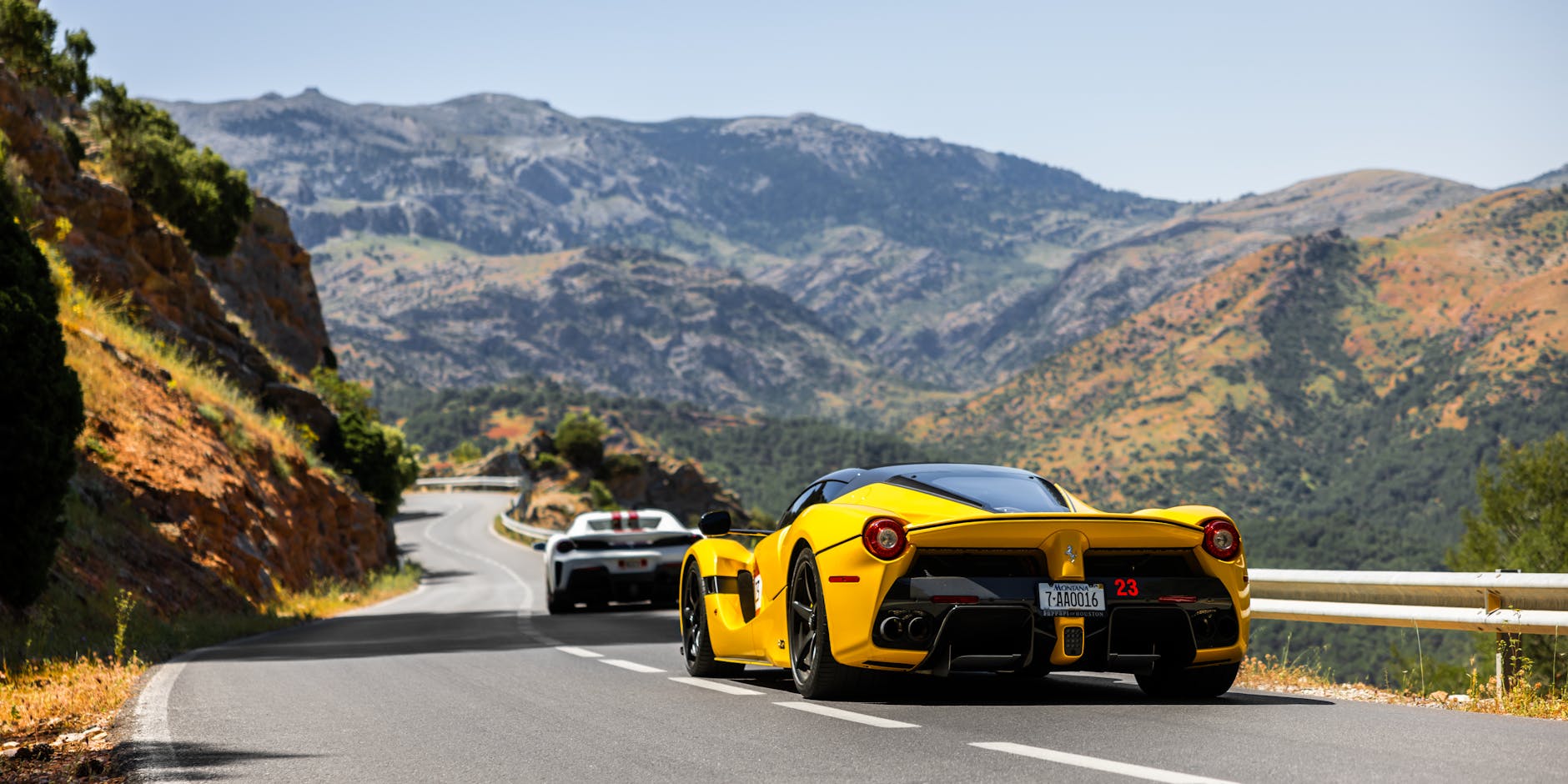 Dwa luksusowe auta sportowe jadą górską, krętą szosą za dnia