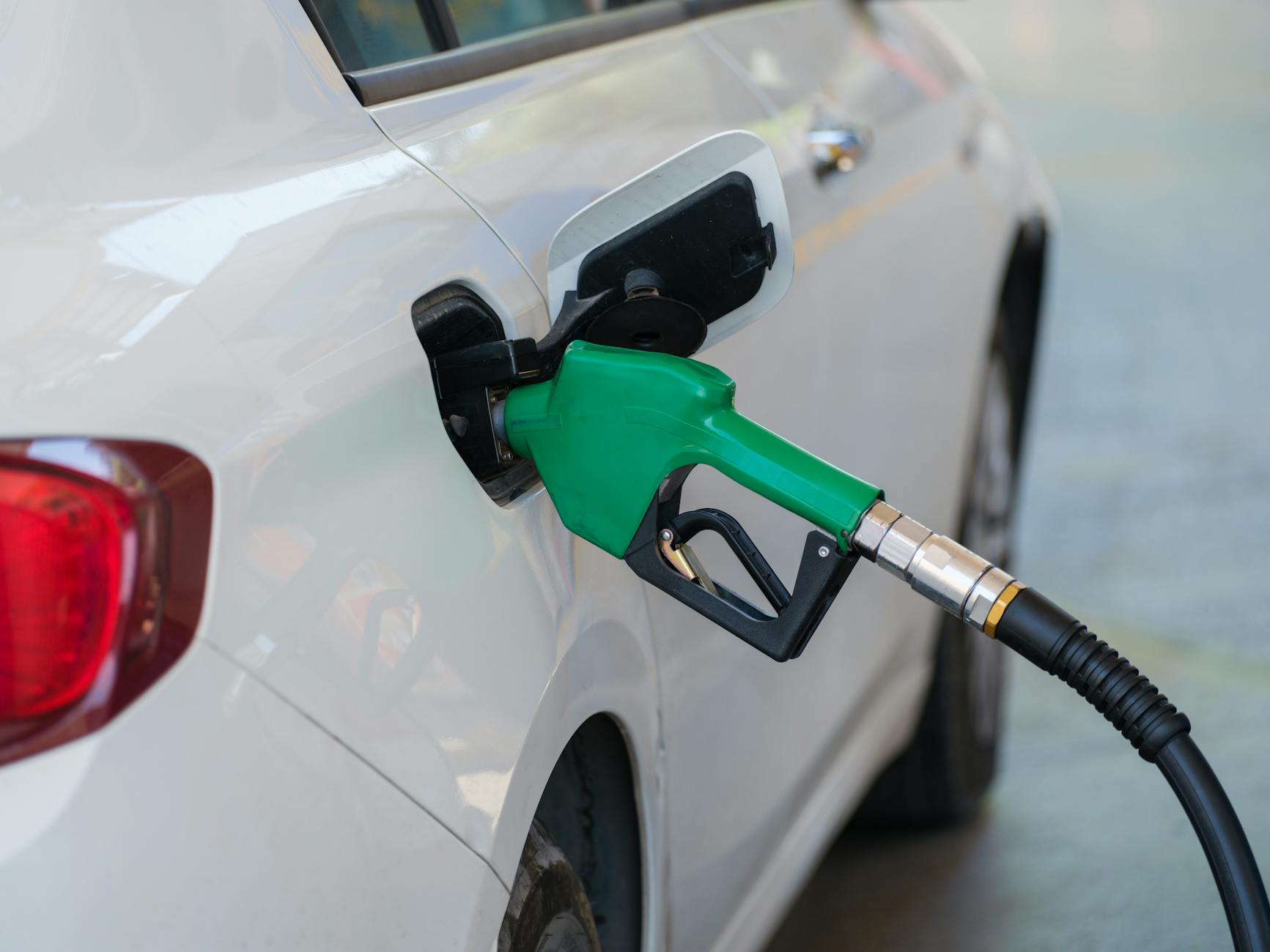 Zielony pistolet dystrybutora tankuje białe auto na stacji paliw