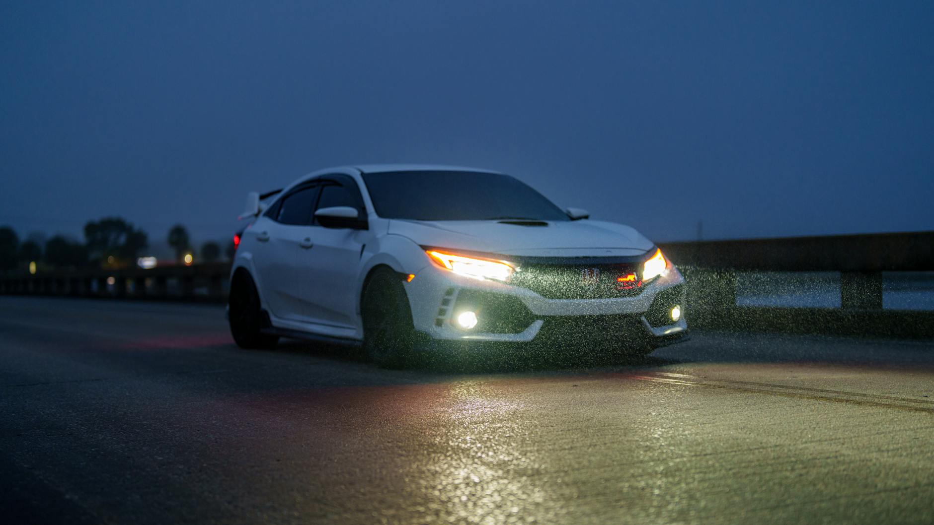 Białe sportowe auto jedzie nocą w deszczu z włączonymi reflektorami