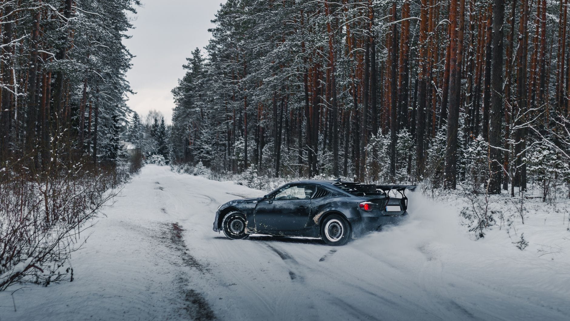 Toyota GT86 driftuje na ośnieżonej szutrowej drodze w zimowym lesie